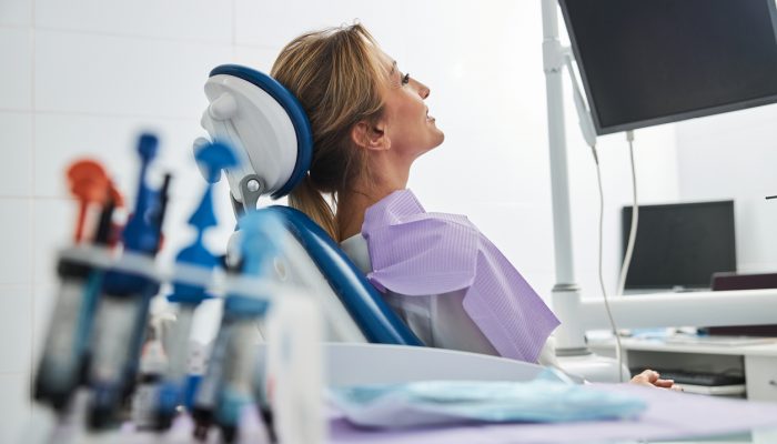 Calm woman patient leaning back on dentist chair and staring at black screen in front of her