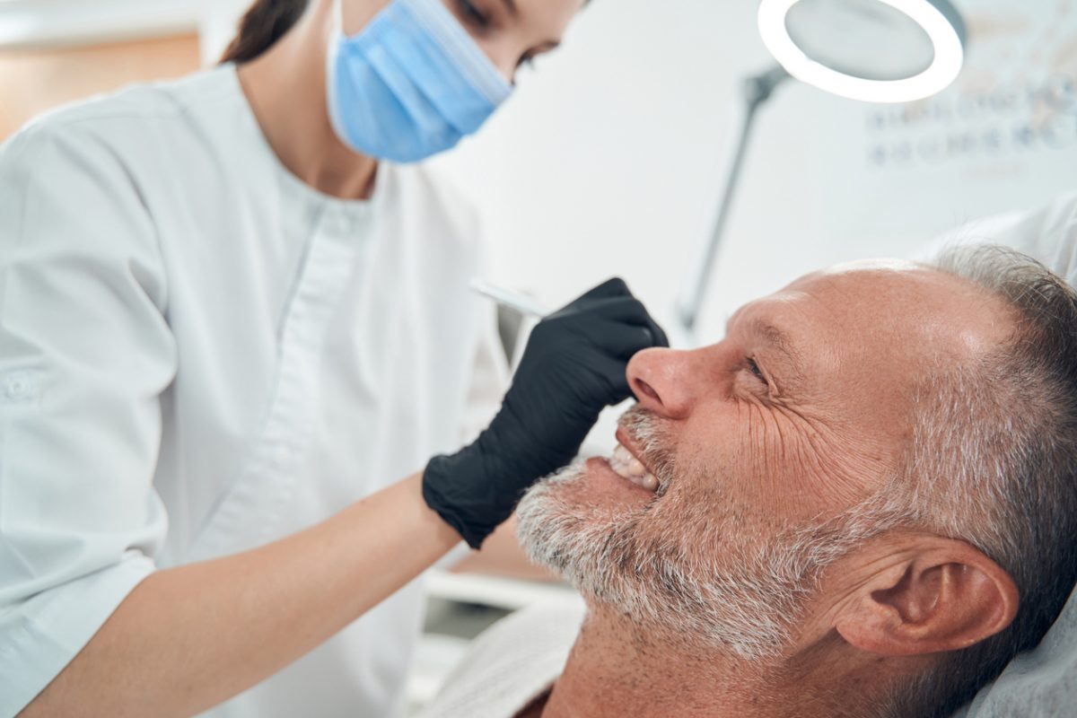 Doctor cosmetologist in medical mask cleaning male face with cleansing tool while man smiling