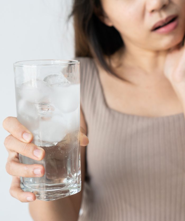 Asian woman feeling teeth pain. Closeup of sad girl suffering from toothache after drinking ice water on white background. Dental health and care, teeth problem concept. Copy space