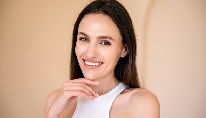 studio shot of young smiling woman with healthy radiant skin looking at camera and touching her chin. eyebrow lamination, skincare concept