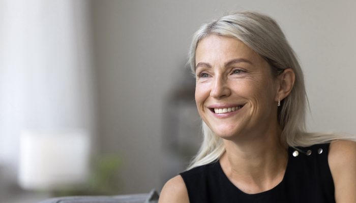 Attractive good-looking middle-aged woman spend time at home sit on armchair staring into distance deep in pleasant thoughts and aspirations, planning bright future at new own apartment. Leisure, rest