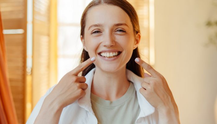 Woman showing her perfect smile pointing her fingers at her teeth, dental care and beauty concept