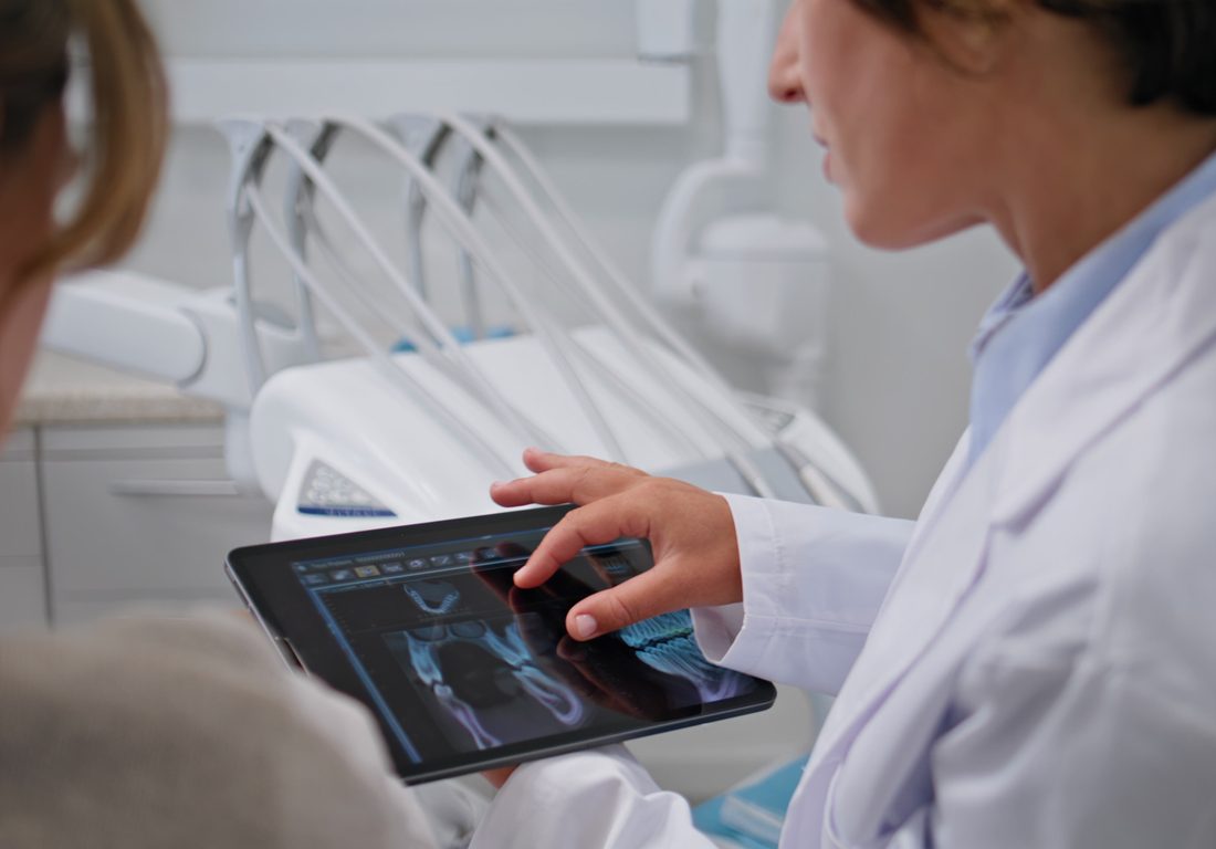 Dentist showing dental x-rays on tablet at stomatology consultation closeup. Woman stomatologist providing detailed analysis of oral health with digital tools. Female patient listen medical explaining