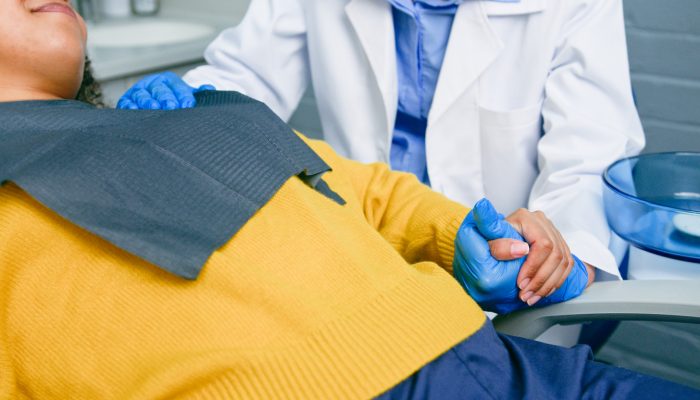 A dentist warmly holds a patient's hand during a dental appointment in a comfortable clinical setting. This moment portrays care, trust, and collaboration, emphasizing empathetic healthcare experiences in a modern dentistry environment.