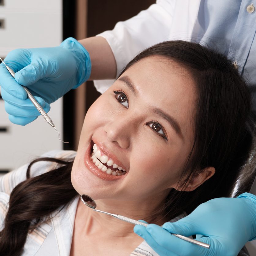 Close-up shot of beautiful Asian female face, white teeth, and cheerful face in dentist's hand, dental treatment with tooth whitening and cleaning in doctor hospital clinic, oral hygiene healthcare.