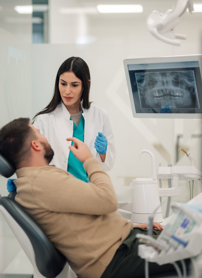 Female dentist discussing dental radiography with male patient seated in dental chair, enhancing understanding of oral health and treatment options