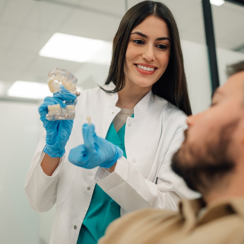 Female dentist explaining to male patient the benefits of dental implants using a model of a jaw