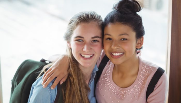 Portrait of schoolgirls embracing each other in corridor at school