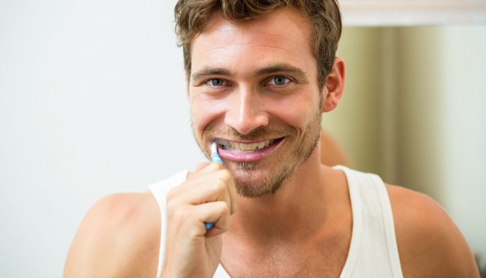 Portrait of young man brushing his teeth in bathroom