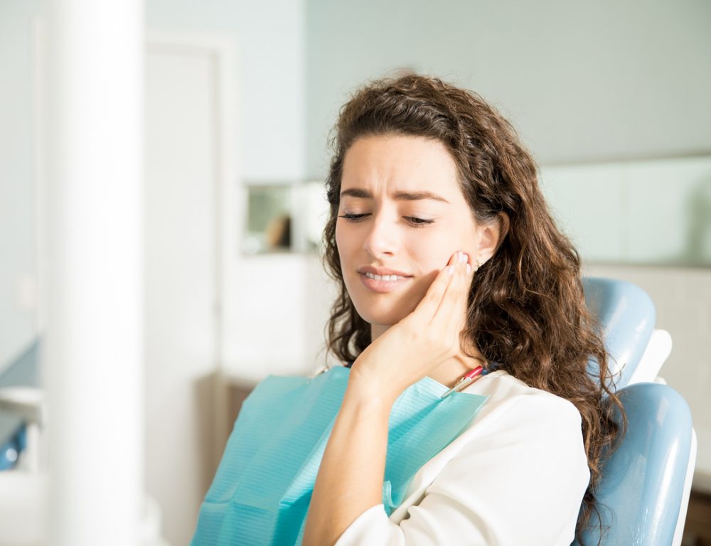 Young woman suffering from toothache while sitting on dental chair in clinic